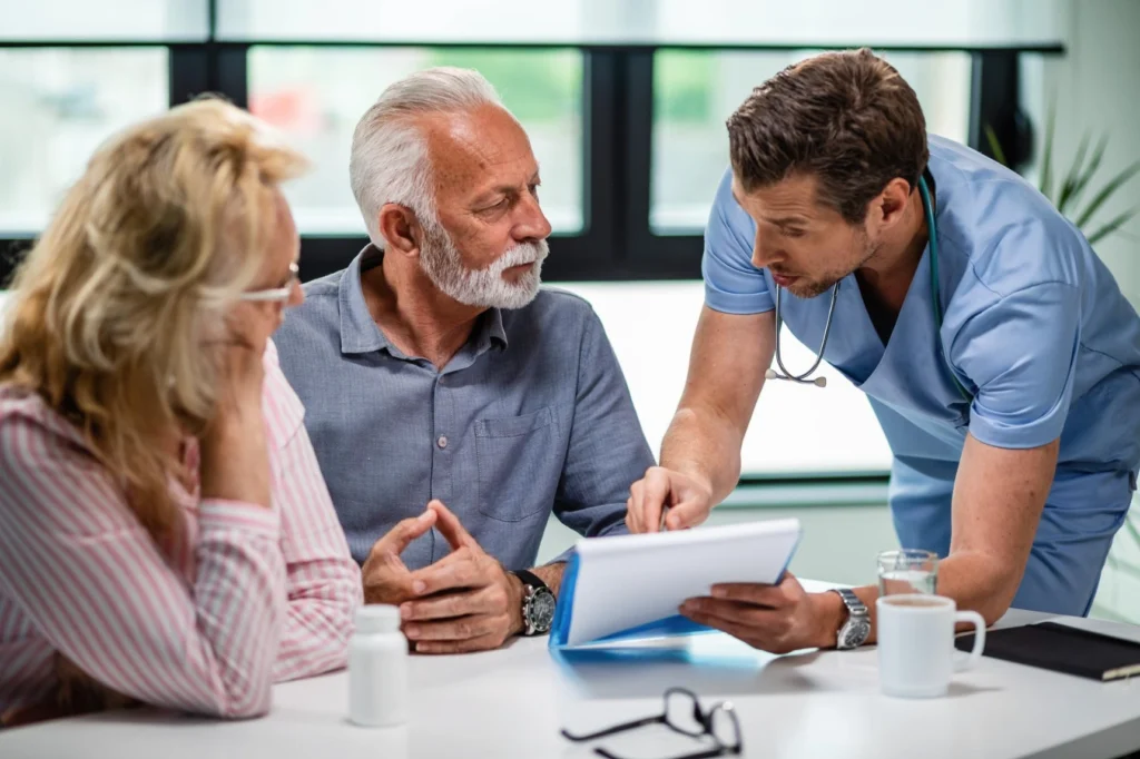 Doctor showing medical documents to concerned elderly couple during consultation.