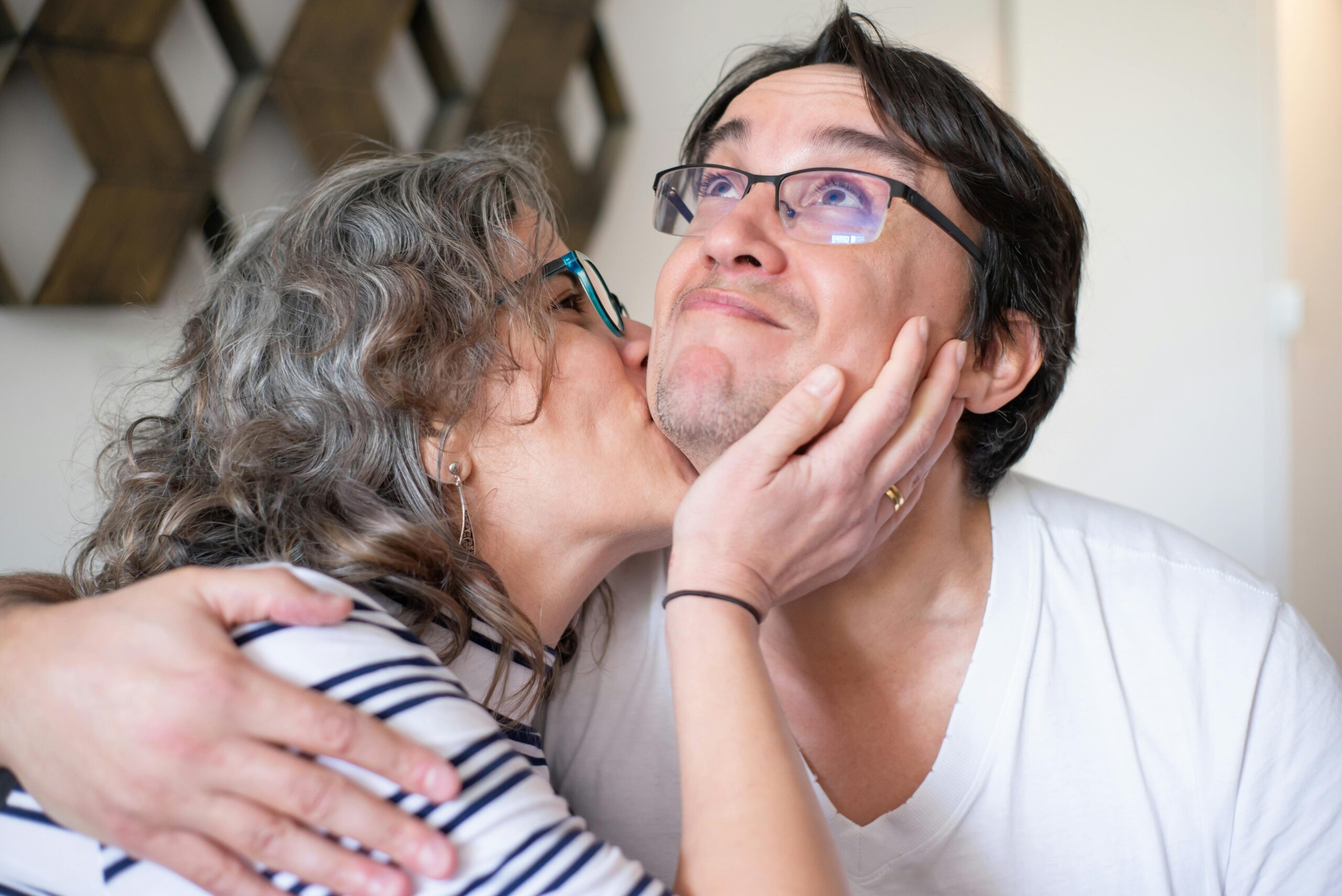 Woman kisses man’s cheek while he smiles and hugs her affectionately.